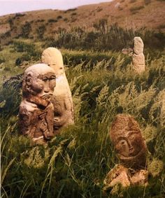 several stone statues in the grass near some hills