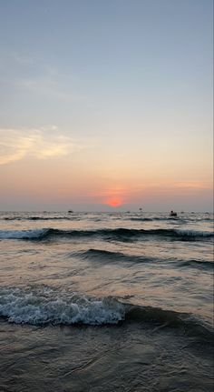 the sun is setting over the ocean with waves coming in to shore and boats out on the horizon