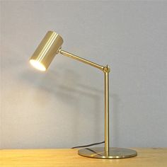 a gold desk lamp sitting on top of a wooden table next to a white wall