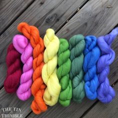 six skeins of yarn in different colors on a wooden surface with text overlay that says the fun thimble