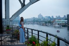 a woman in a blue dress is standing on a balcony overlooking the water and boats