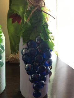 two vases with grapes and leaves in them on a table next to each other