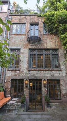 an old brick building with lots of windows and furniture in the courtyard area, surrounded by greenery