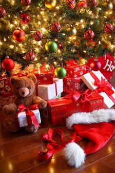 a teddy bear sitting next to presents under a christmas tree