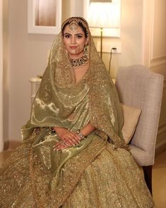 a woman in a green and gold wedding dress sitting on a chair wearing a veil