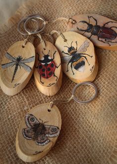 four wooden spoons with bugs painted on them and one is holding a pair of scissors