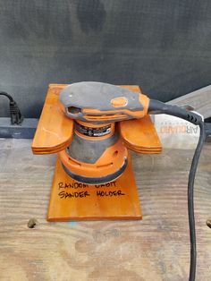 an orange sander sitting on top of a wooden table next to a black hose