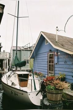 a sailboat docked in front of a blue house with flowers growing on the deck