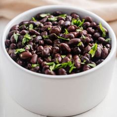 a white bowl filled with black beans and garnished with green leaves on top