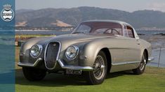 an old silver car parked on top of a lush green field next to the ocean