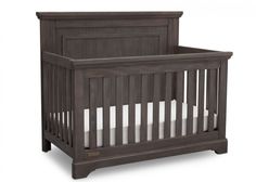 a wooden crib with white sheets on the bottom and side rails, in dark wood