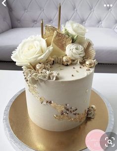 there is a white cake with gold decorations on the top and flowers on the bottom