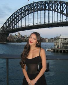 a beautiful young woman standing in front of a bridge