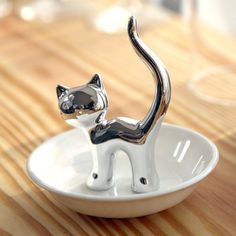 a silver cat figurine sitting in a white bowl on a wooden table top