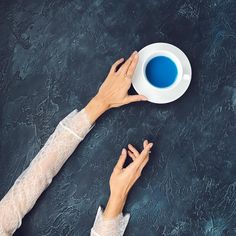 two hands holding a white plate with blue liquid in it on a black table top