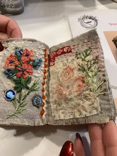 a hand holding an open book with embroidered flowers on it and buttons attached to the cover