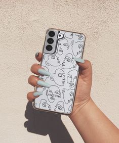 a woman's hand holding an iphone case with cartoon faces on it and blue nail polish