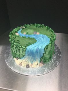 there is a cake with green and blue icing on the top that has a river running through it