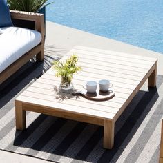 a coffee table with two cups on it next to a couch near the water's edge