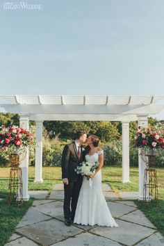 a bride and groom kissing in front of an outdoor wedding ceremony arch with red flowers