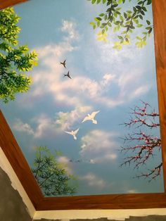 the ceiling is painted with birds flying in the blue sky and green leaves on it