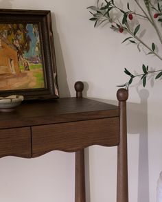 a table with a bowl on it next to a painting and vase filled with flowers