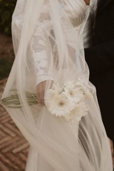 the bride and groom are dressed in white for their wedding day, holding each other's bouquet