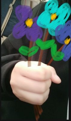 a person holding flowers in their hands with the stems painted purple, blue and green