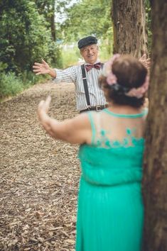 an older man and woman standing next to a tree in the middle of a forest