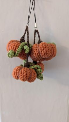 three crocheted pumpkins hanging from strings on a white wall, one is orange and the other is green