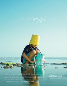 a boy in a yellow hat is sitting on the beach and holding a blue bucket