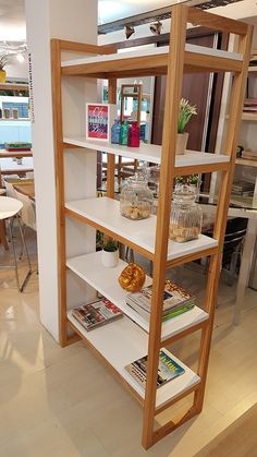 a shelf with books, magazines and vases on it in a room filled with furniture