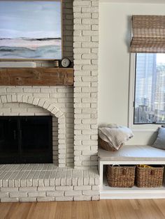 a living room with a brick fireplace and white painted walls, filled with baskets on either side of the fire place