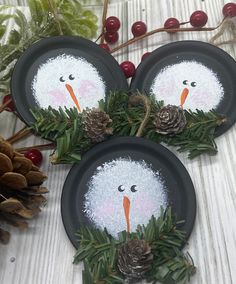 three black plates decorated with snowmen and pine cones on top of a table next to evergreen branches