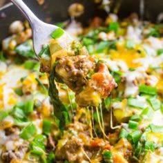 a spoon full of food that is being lifted from a skillet with cheese and vegetables