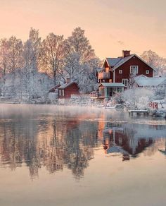 a red house sitting on top of a lake next to a snow covered forest filled with trees