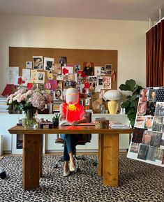 a woman sitting at a desk with flowers and pictures on the wall