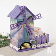 a small house with a windmill on top of it and flowers in the foreground