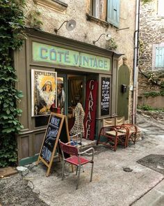 an old fashion store front with chairs and signs in the window, on a cobblestone street