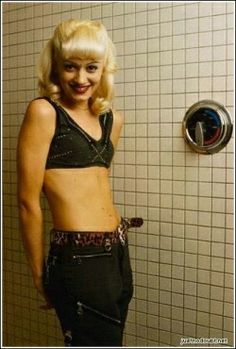 a woman standing in front of a shower with no shirt on and her pants rolled up