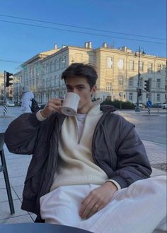 a man sitting on a bench drinking from a cup