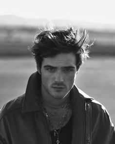 a black and white photo of a young man with long hair wearing a leather jacket