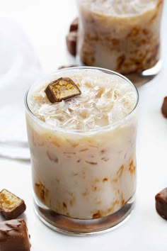 two glasses filled with ice and chocolate on top of a white table next to other desserts