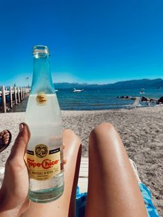 a person sitting on the beach with a bottle of beer