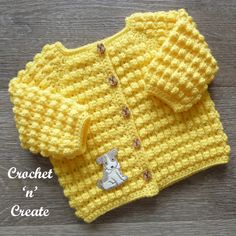 a crocheted sweater with a teddy bear on the front and chest, sitting on top of a wooden surface