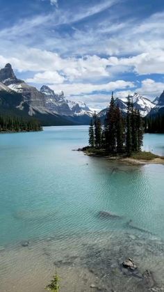 an island in the middle of a lake surrounded by trees and mountains with snow on top