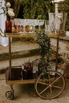 a bar cart filled with glasses and bottles on top of a stone floor next to steps