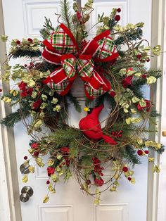 a christmas wreath on the front door with a red bird hanging from it's side