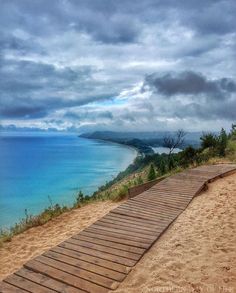 a wooden walkway leading down to the beach on a cloudy day with blue water in the background