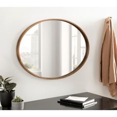 a round mirror hanging on the wall next to a potted plant and coat rack